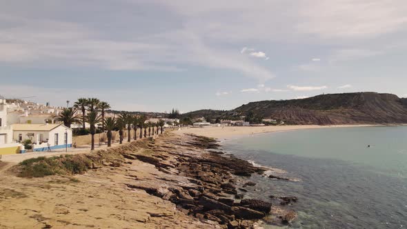 Low fly-over along Rocky shore to pristine Praia da Luz Coastline. Aerial alt