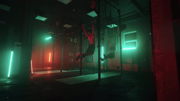 Physical Exercise in Dark Gym  Man and Woman are Doing Pullups Fitness Club or Training Base alt