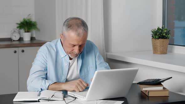 A Tired Elderly Man Leaning on His Arm Sleeps Indoors During the Working Day