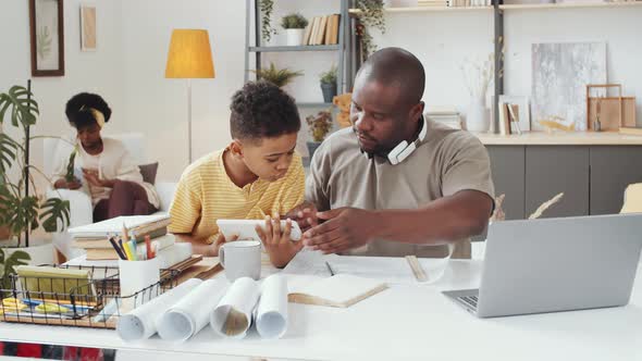 Afro-American Architect Working at Home and Helping Little Son with Tablet alt