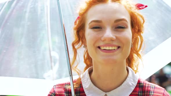 Red haired freckled female smiling at camera holding umbrella alt