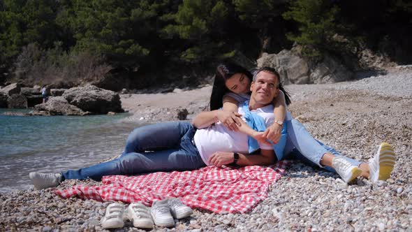 Husband and wife spend the weekend, hugging and having picnic near sea on sunny summer day. alt