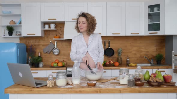 Pregnant Woman Cooking Food Looking For A Recipe On Laptop In Kitchen alt