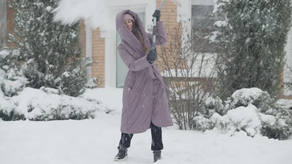 Joyful Slim Charming Woman Cleaning Snow with Shovel and Spinning Laughing Outdoors alt