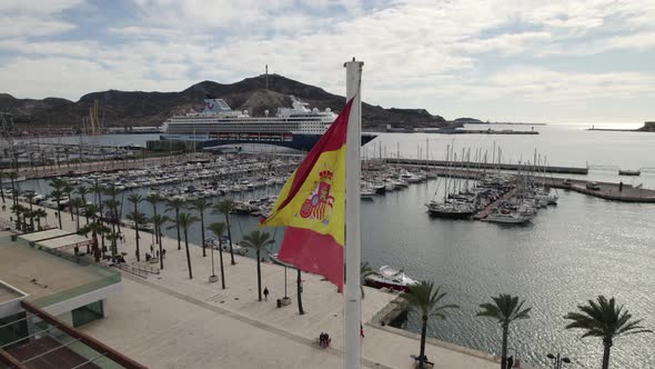 Spanish flag sways in the wind, Cartagena marina, Spain. Aerial Orbiting
