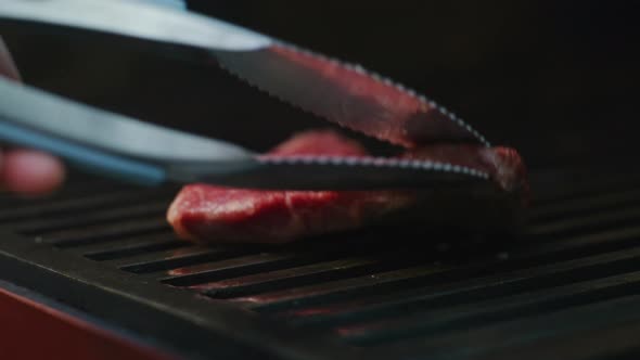 Chef Turns Meat on Grill with Tongs