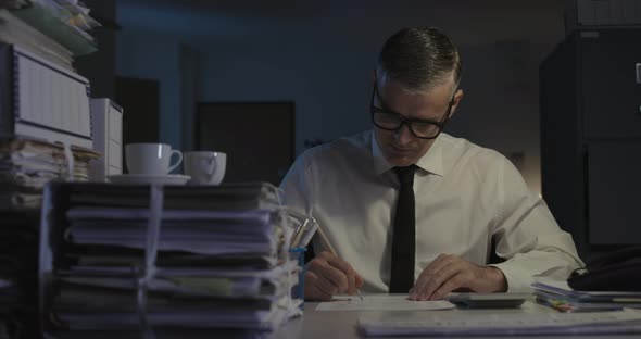 Businessman sitting at desk and working late at night, he is using a calculator