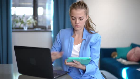 Front View Concentrated Caucasian Young Woman Messaging Online on Tablet Surfing Internet on Laptop alt