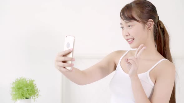 Beautiful young asian woman sitting taking a selfie with smart phone on bedroom. alt