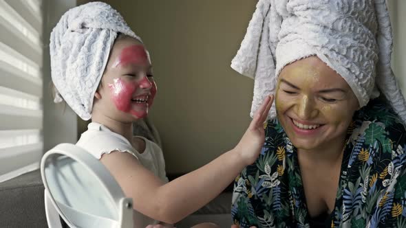 Little Girl with a Cosmetic Mask on Her Face Helps Her Mother To Make a Cosmetic Mask alt