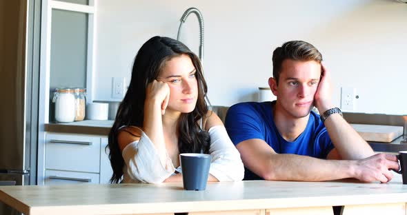 Thoughtful couple sitting in kitchen alt