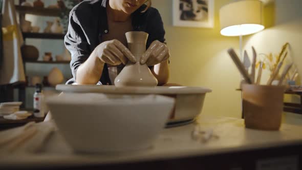 Young Female Potter Pulls the Neck of an Earthenware Vessel on Potter's Wheel
