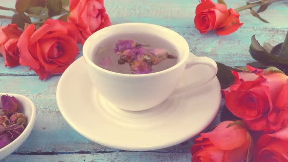 White cap of  tea with fragrant dried rose buds, fresh rose flowers. Tea brewing. alt