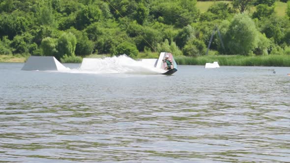 Athlethic Male Wakeboarder Doing Back Flip and Other Tricks Near Ramps alt