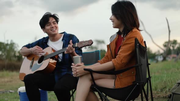 A happy young Asian couple backpacker playing the guitar and singing a song together.