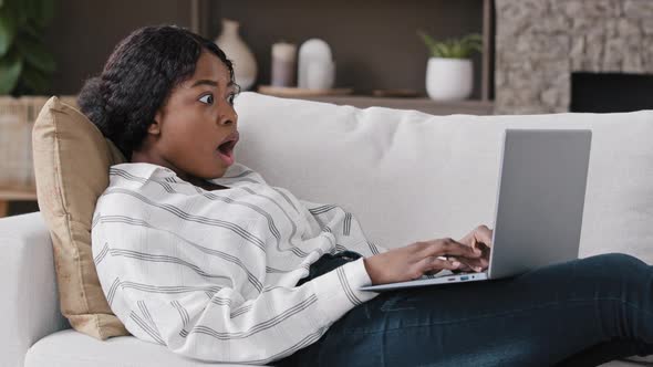 African Girl Freelancer American Biracial Woman Lying on Couch at Home Looking in Laptop Reading alt