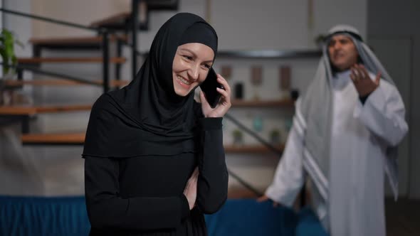 Cheerful Middle Eastern Woman Talking on Phone Smiling Ignoring Unsatisfied Man Talking at alt