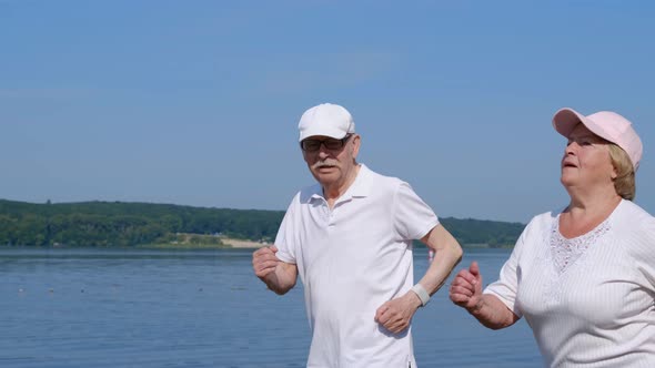 Senior couple running outdoors. In the morning, retirees run to the park near the lake alt