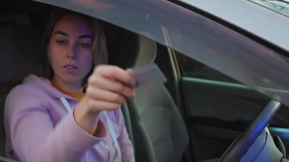 Woman sits behind wheel the right-hand drive of a car and submits documents to a policeman alt