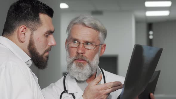 Senior Male Doctor and His Colleague Discussing Xray Scans of a Patient alt