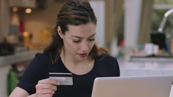 Young adult woman buying online using laptop in kitchen