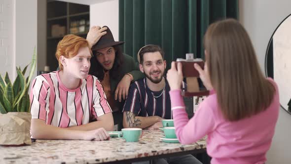 Woman Photographing Men on Retro Camera in Vintage Coffee Shop alt