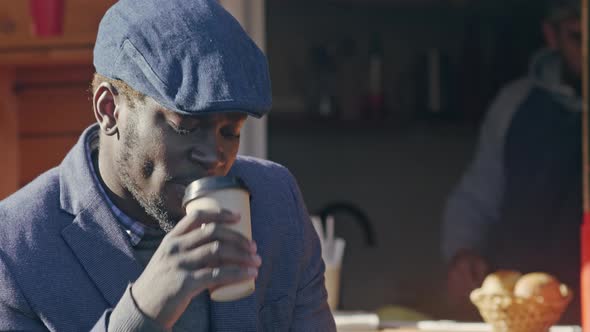 African American man drinking coffee near coffee-shop