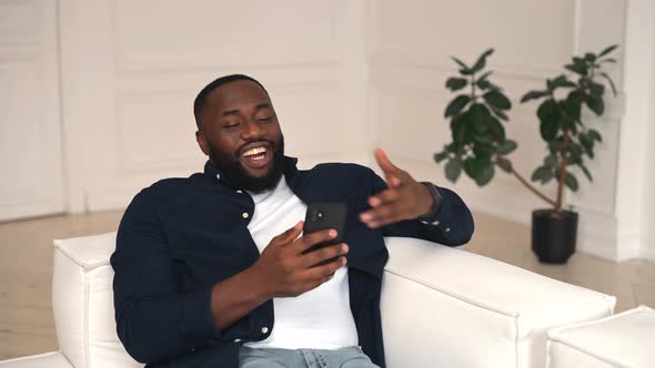 Excited AfricanAmerican Guy Holding Mobile Phone and Greeting Online Interlocutor alt