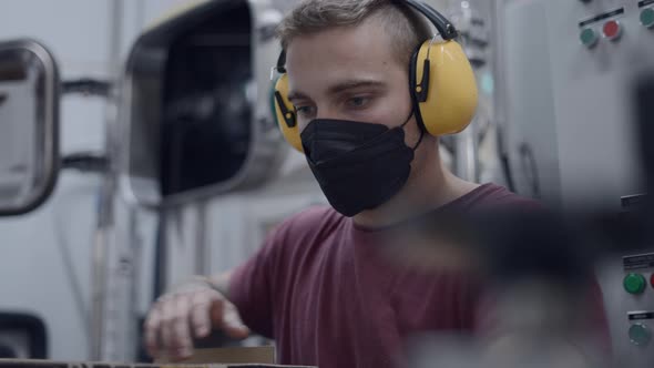 A Young Worker With Noise Reduction Ear Muff And Facemask Filling A Box With Canned Beers alt