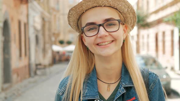 portrait of a happy beautiful blond girl with glasses, a hat and a blue jeans jacket.