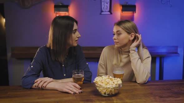 Two Girlfriends in Pub at Bar Counter Drink Beer and Talking with Each Other