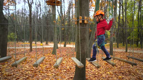 Little girl in orange helmet and protective gear on rope-way in autumn  forest. rope park.