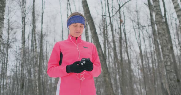 A Young Woman on the Morning Jog Holds in Her Hands a Smartphone Picks a Music Track for Training alt