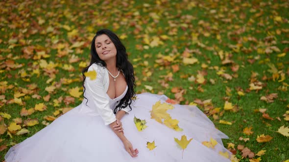 Stunning Bride is Posing on Lawn in Park in Fall Day Yellow Leaves are Falling on Her Figure alt