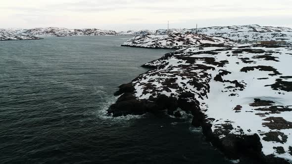 The Drone Flies in the Black Waters of the Ocean That Wash the Rocky Shore Covered with Snow