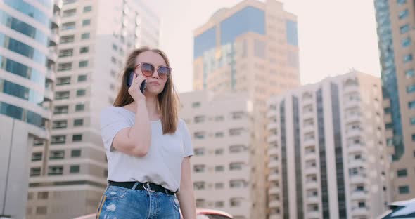 Young Beautiful Woman Talking on the Phone on the Background of Buildings alt