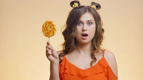 Cute girl with caramel candy on colored studio background alt