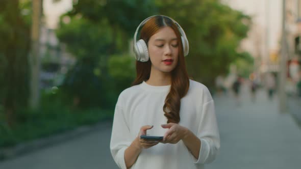 Happy Asian woman in headphones walking in the city street outdoor having fun listening to music