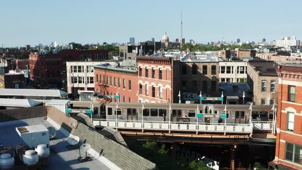 A slow aerial reveal of the Chicago skyline beyond train station as a rail trail departs. alt