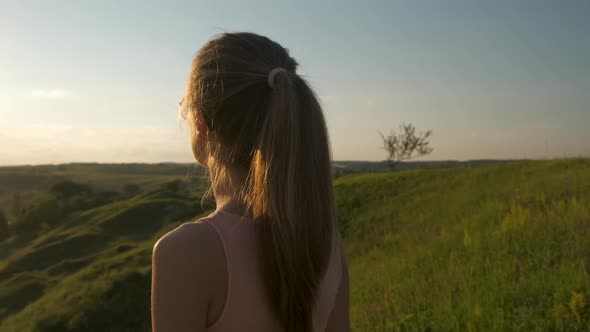 Young woman standing in green field looking at sunset view in evening nature. Relaxation and  alt