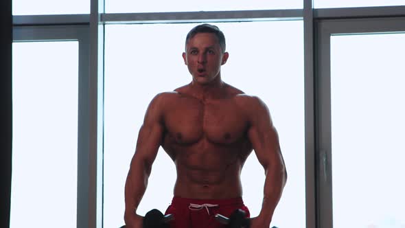 Sports Training in Studio with Panoramic Windows Shirtless Athletic Man Pumping His Hands Muscles alt