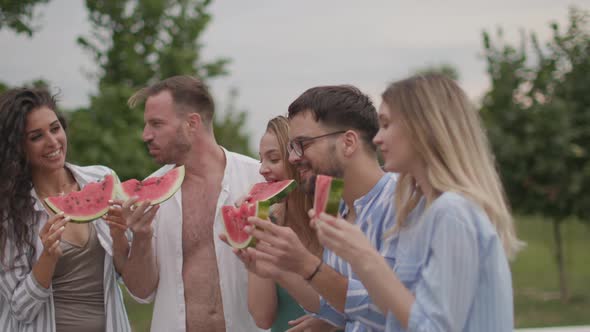 Group of young people standing by the swimming pool and eating watermelon in the house backyard