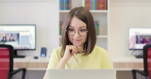 Young Woman is Smiling Sitting at a Desk with a Laptop Working in the Library alt