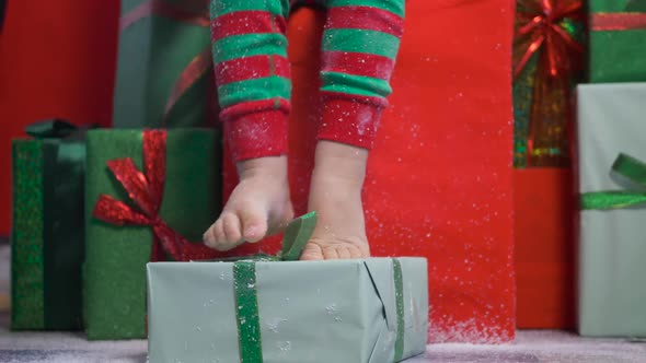 Child in a Green Dwarf Costume Sits on Gift Boxes with Deer Antlers alt