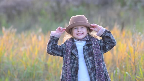 Cute little girl in a coat and hat walks on the meadow