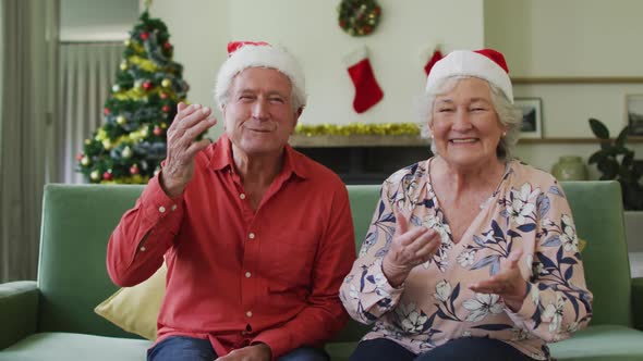Happy caucasian senior couple in santa hats on video call at christmas time alt