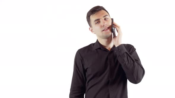 Laughing Young Man in Black Shirt Talking By Mobile Phone Over White Background alt