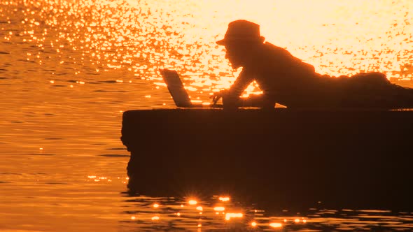 Freelancer Typing on Laptop Over Sunset Reflecting in Sea Water. Male, Blogger with Laptop on the