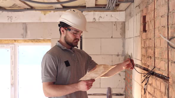 A builder in a hard hat examines a construction plan at a construction site.