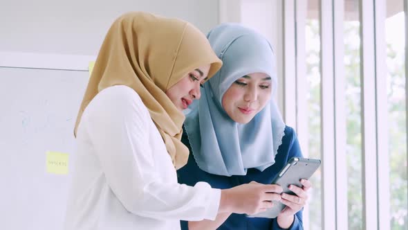 Two young Muslim businesswomen discussing a work in the office. alt